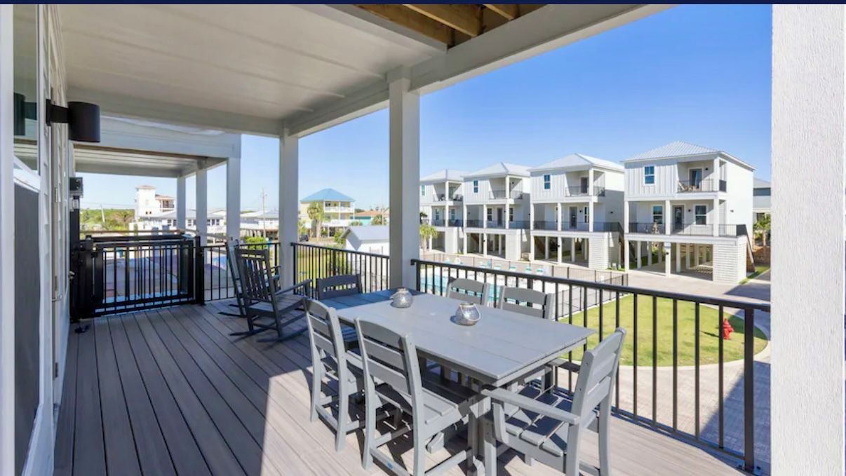 Large covered front porch with dining table and rocking chairs overlooking pool
