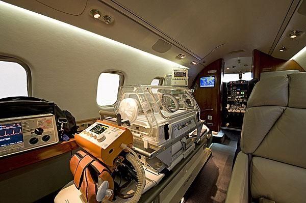 Interior de un avión de evacuación médica con una incubadora de pacientes, equipo médico y panel de control.