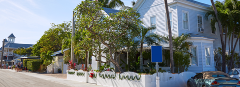 A blue car is parked in front of a white house.