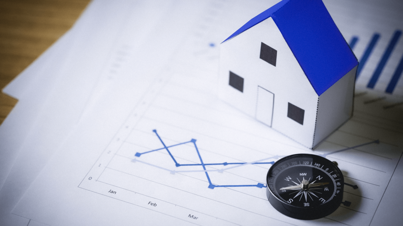 A model house is sitting on top of a graph next to a compass.