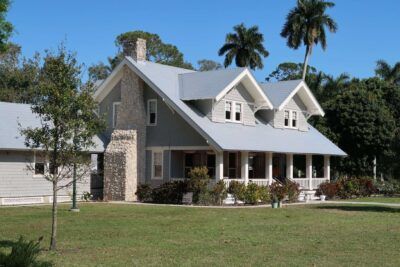 A large white house with a gray roof is surrounded by palm trees