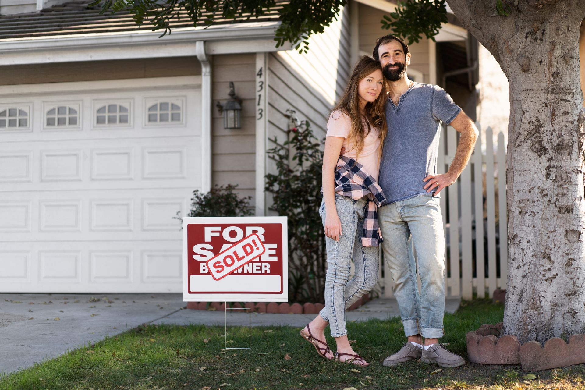 A man and woman are standing in front of a for sale sign.