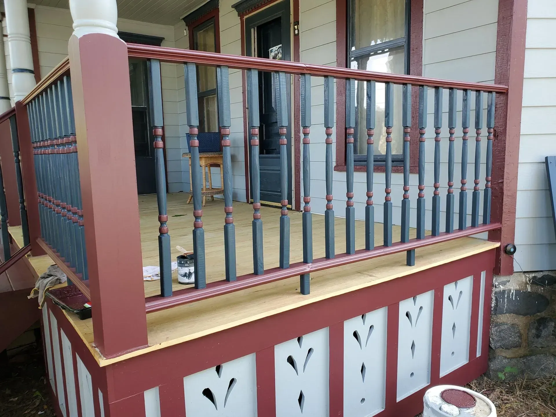 A porch with a wrought iron railing is being painted red and white.