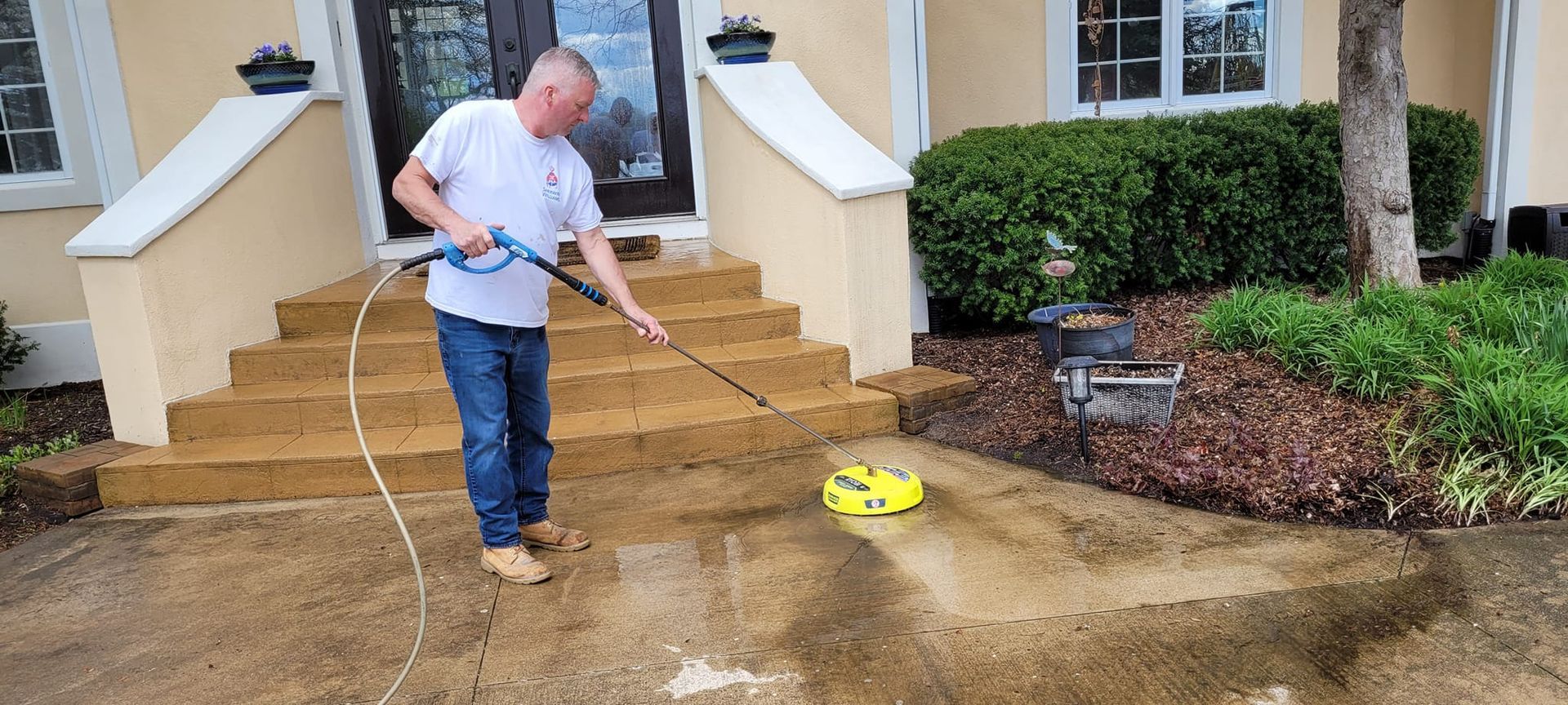 A man is using a pressure washer to clean a driveway in front of a house.