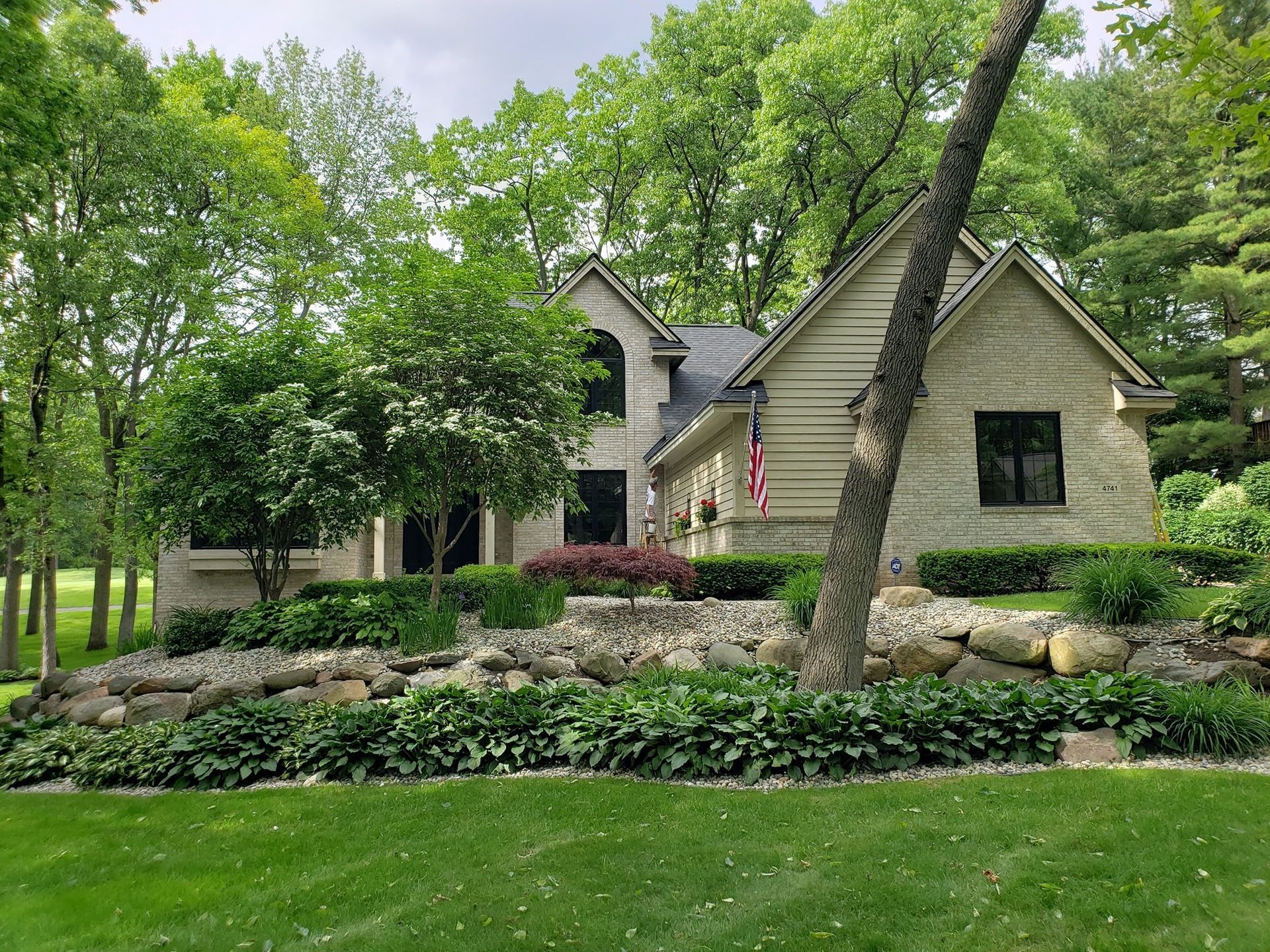 A large brick house with a large lawn in front of it surrounded by trees.
