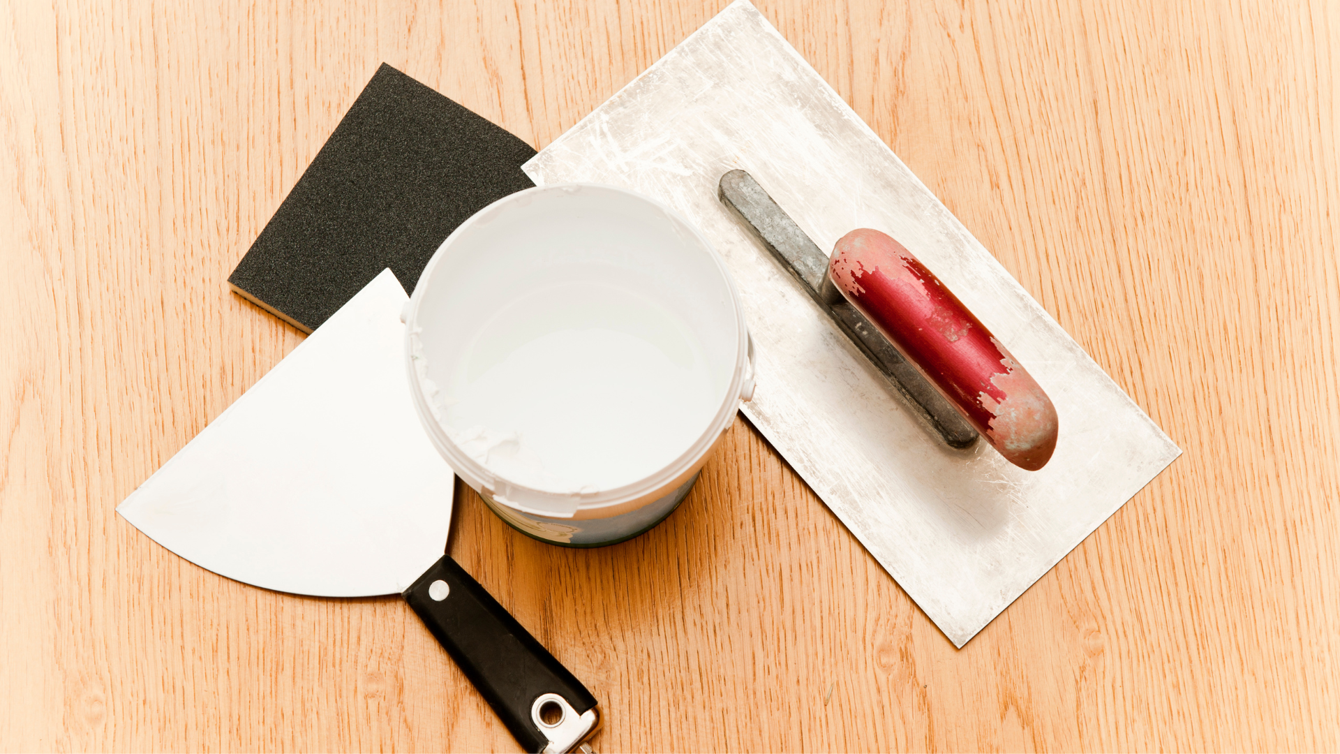 A spatula , trowel , and sandpaper are on a wooden table.