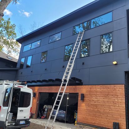 A white van with a ladder attached to the back is parked in front of a large building.