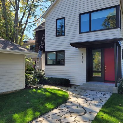 A man is standing on a ladder in front of a white house with a red door
