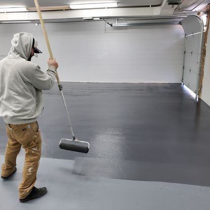 A man is painting a garage floor with a roller.