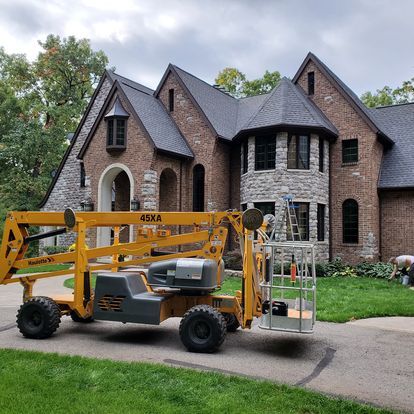 A yellow lift is parked in front of a large brick house.