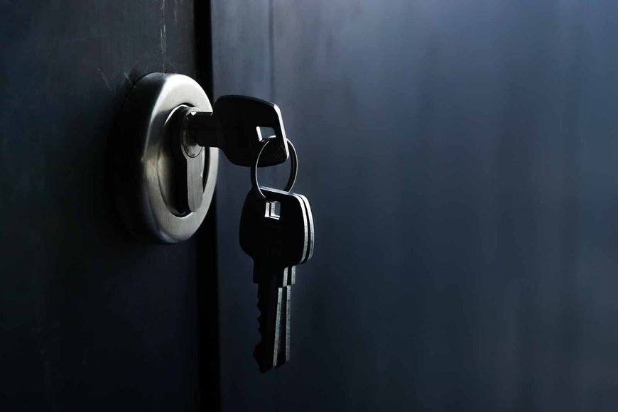 Two keys are in a keyhole on a black door.