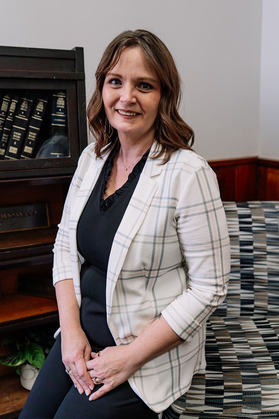 A woman is sitting on a couch in front of a bookshelf.