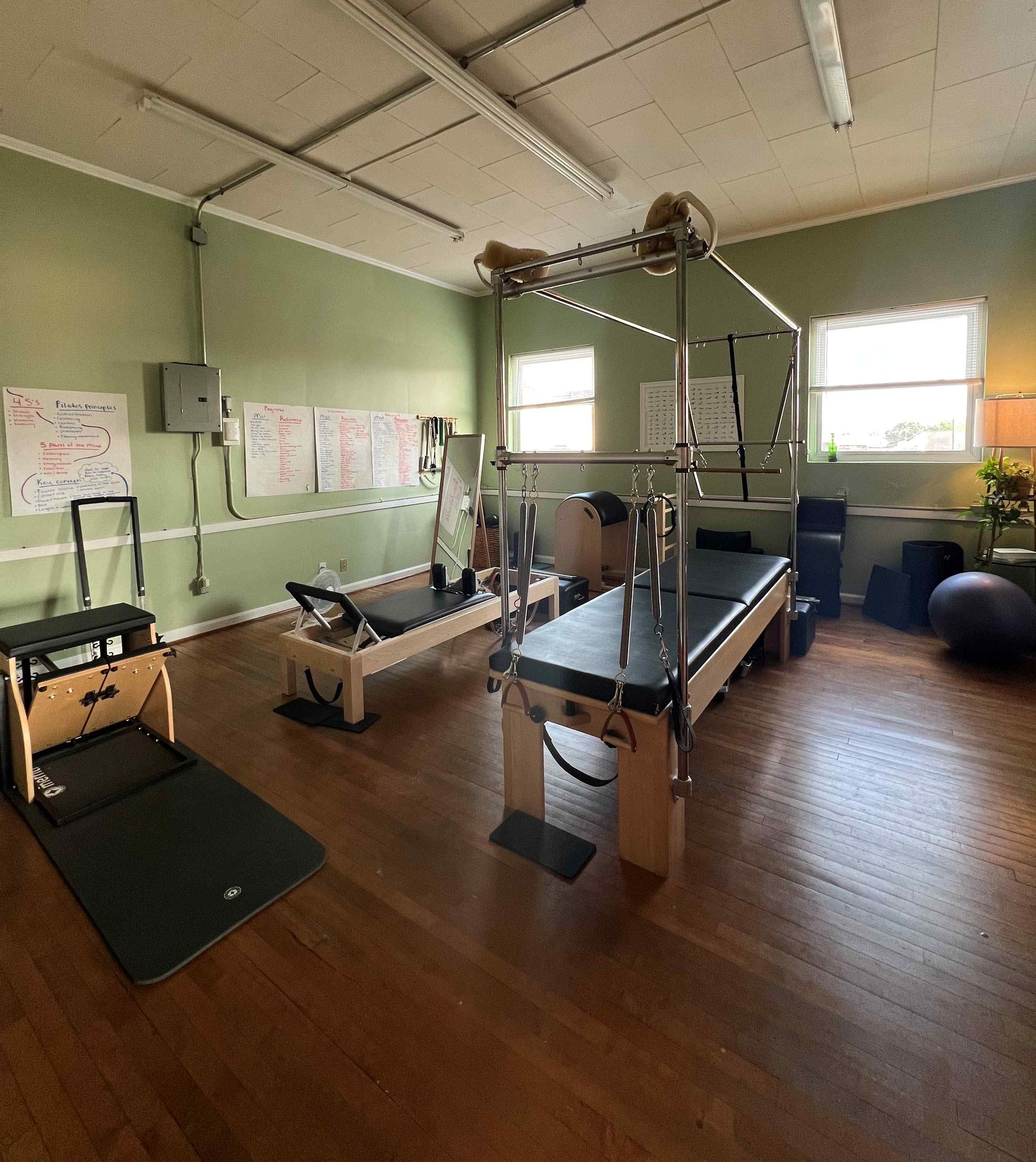 Pilates studio with equipment on a wood floor and green walls.