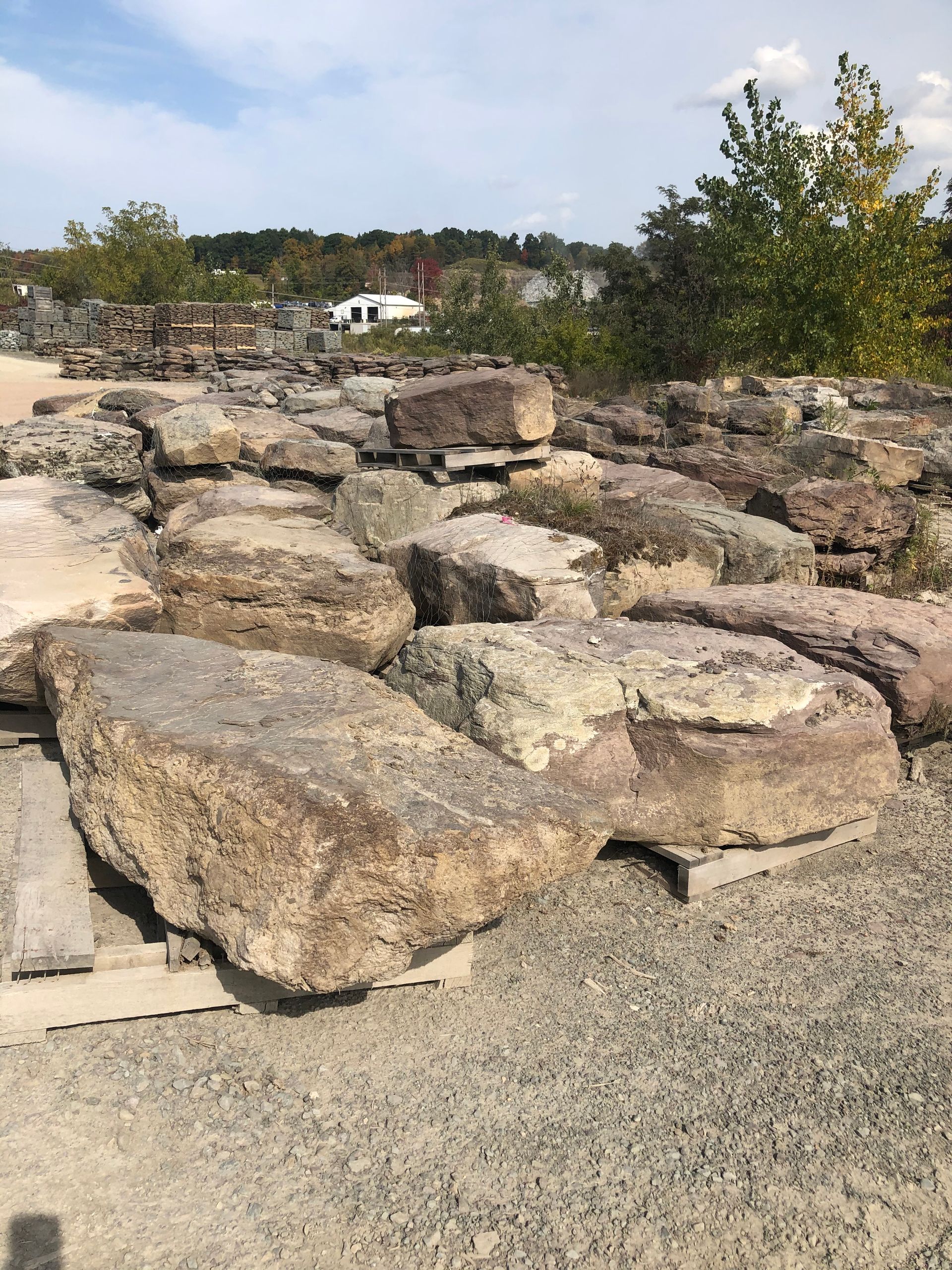 Large, rough-cut stone blocks stacked on wooden pallets in a sunny outdoor yard.
