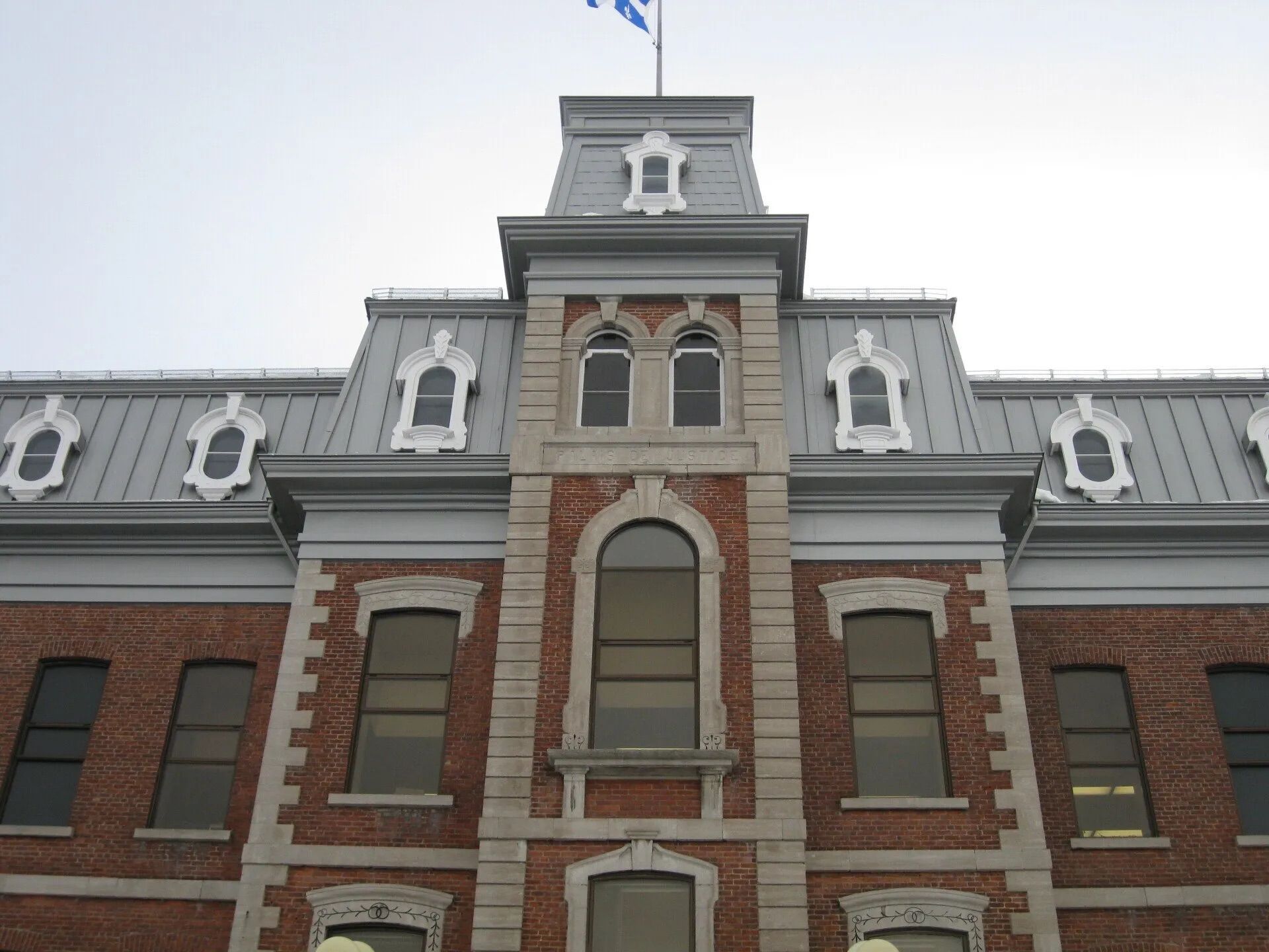 Brick building with gray roof and Quebec flag.