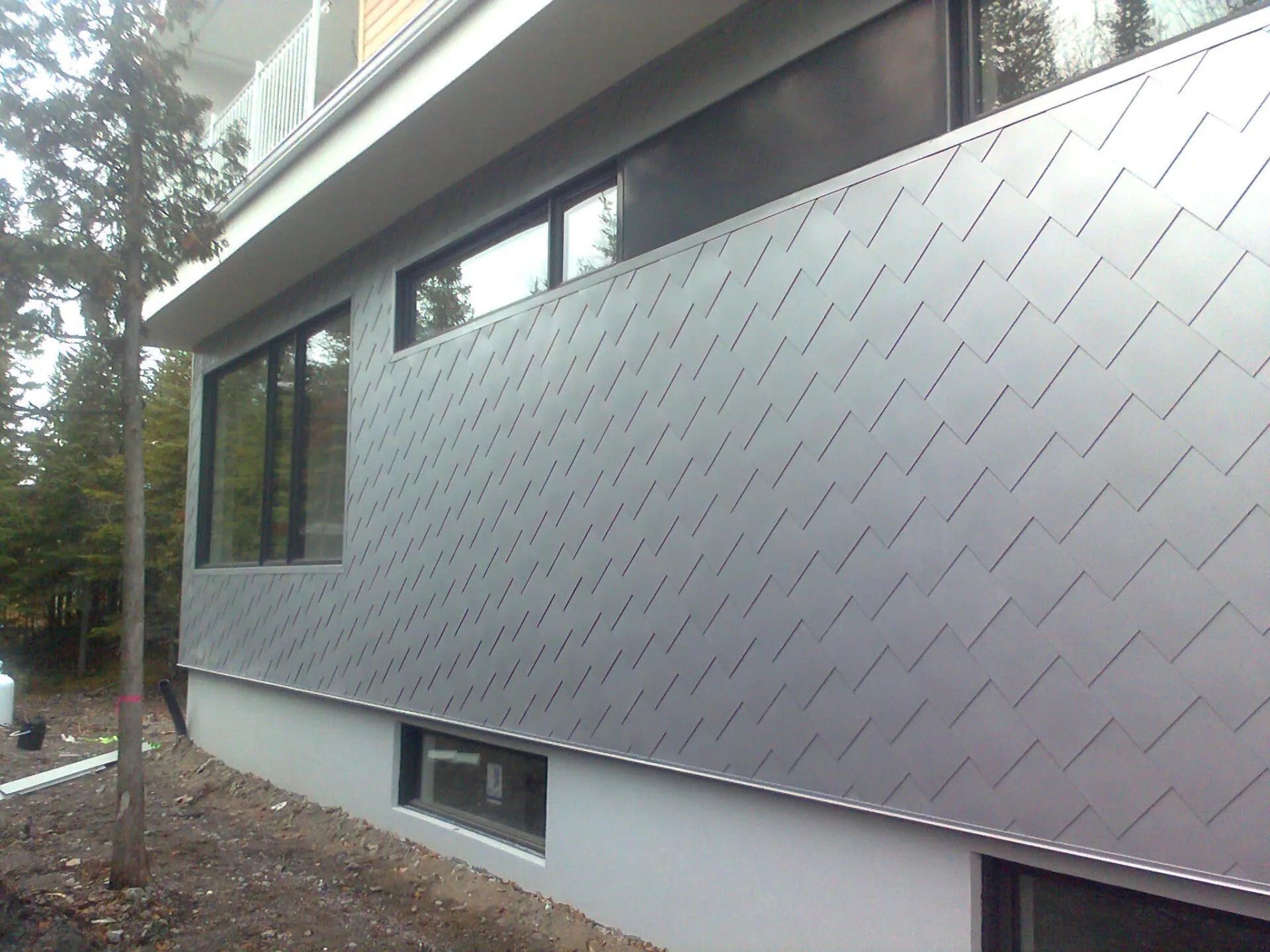 Modern building exterior with gray metal siding in a diagonal pattern and dark windows.