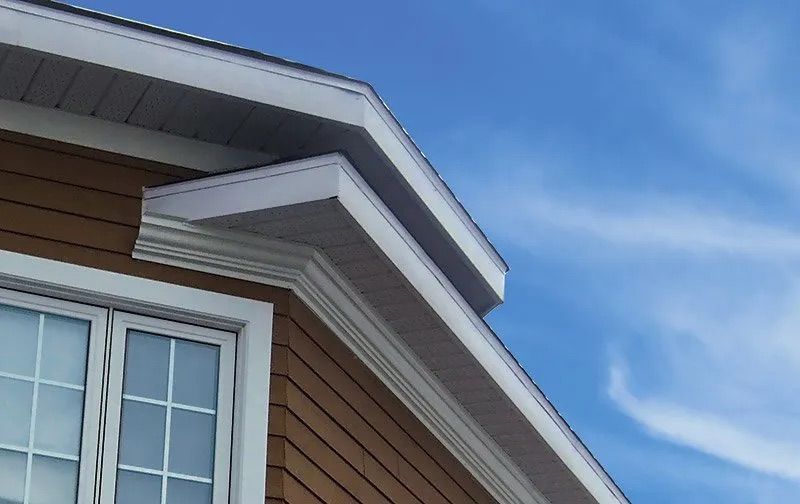Brown siding and white trim on a house with a window, against a blue sky.