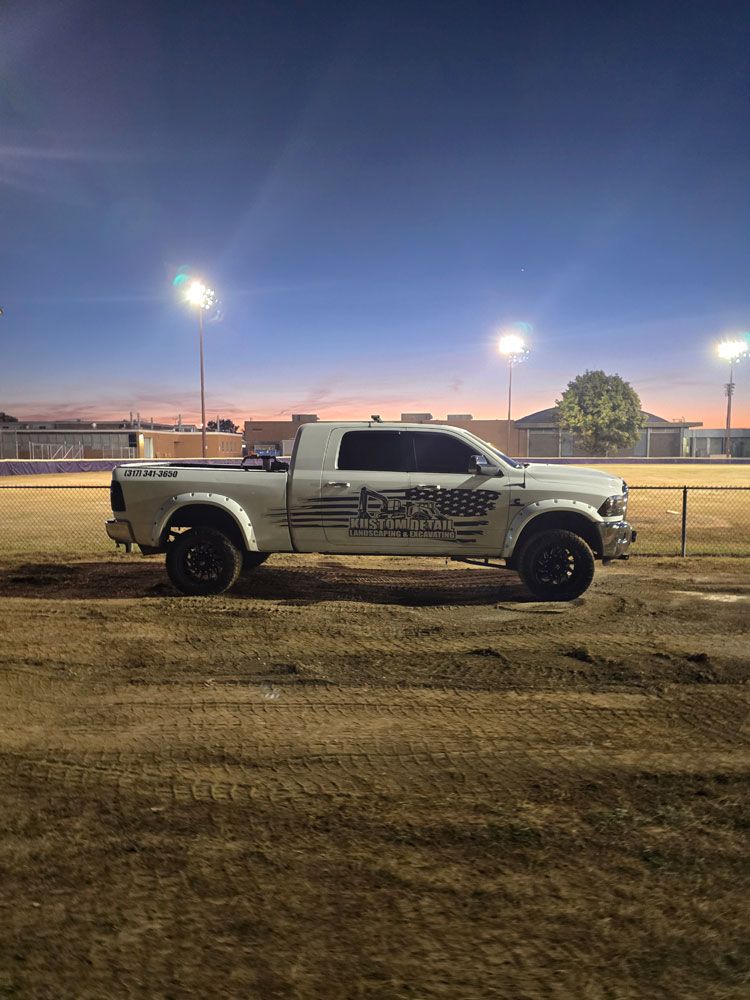 White pickup truck parked on dirt field at dusk under bright lights.