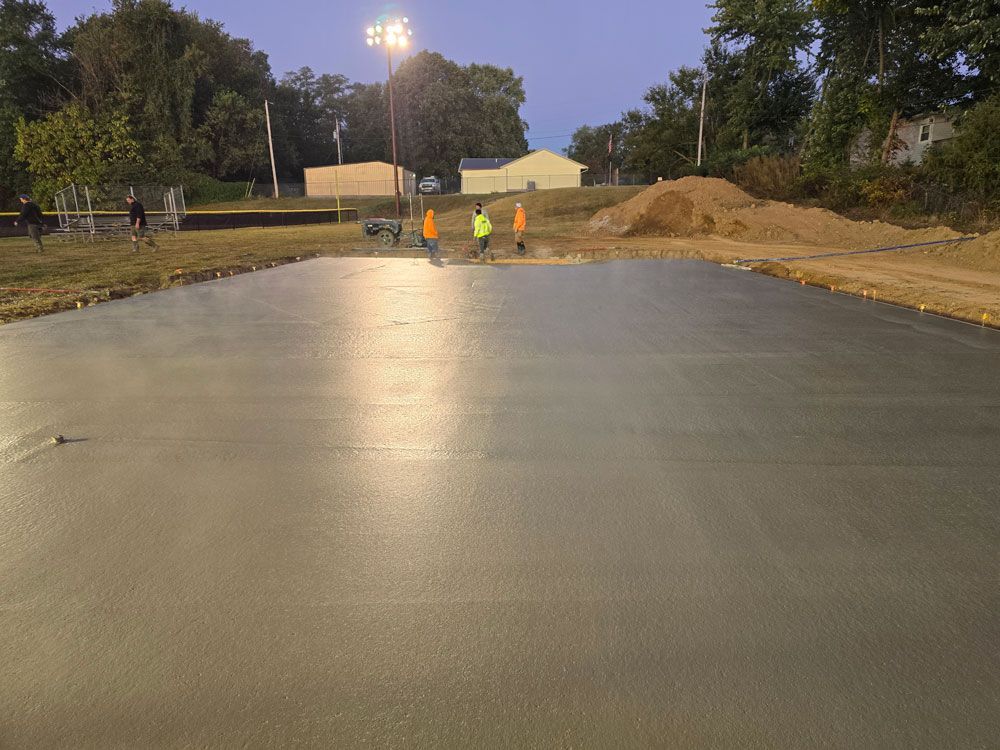 Newly poured concrete surface with workers in orange vests, evening.