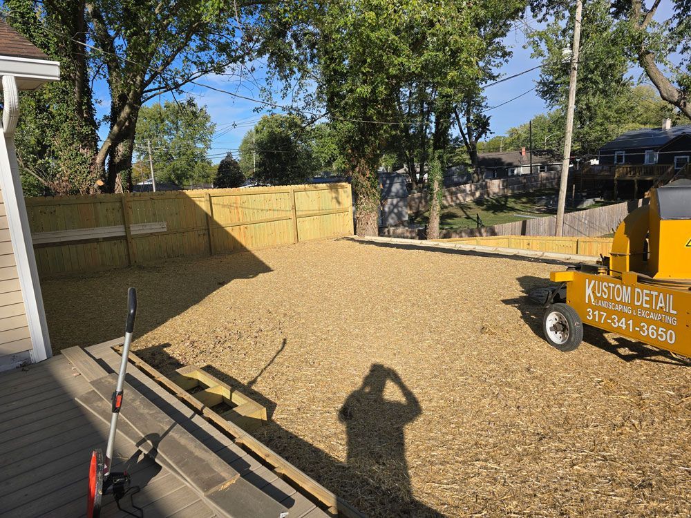 A gray building with black garage doors, an excavator, and black drainage pipes on a gravel lot.