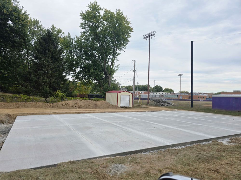 Concrete pad with parking spaces at a sports field under cloudy skies.