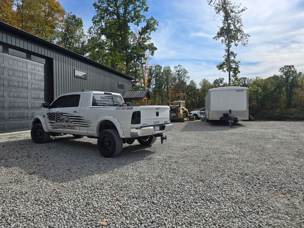 White pickup truck parked on gravel next to a gray building and trailer under a blue sky.