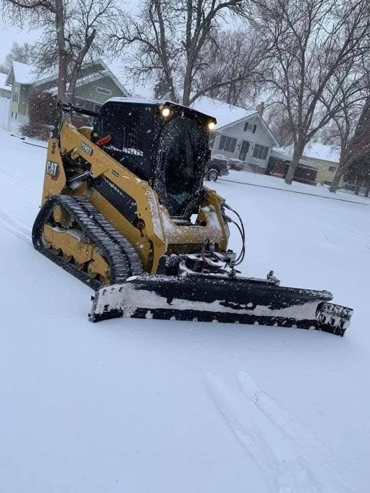 Yellow snow plow clearing snow on a residential street during a snowfall.
