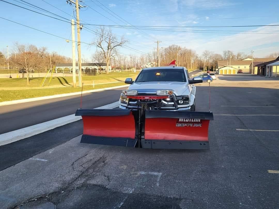 White pickup truck with a red snowplow parked on pavement.
