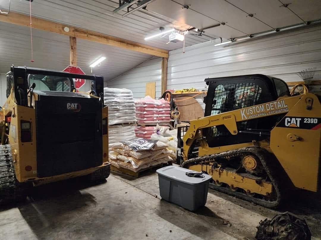 Two yellow CAT skid steer loaders inside a storage building, pallets of bags in the background.