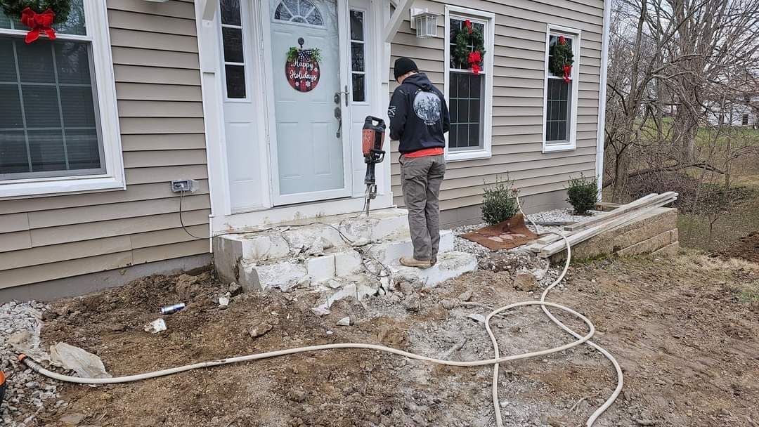 Person using a jackhammer to demolish concrete steps in front of a house.
