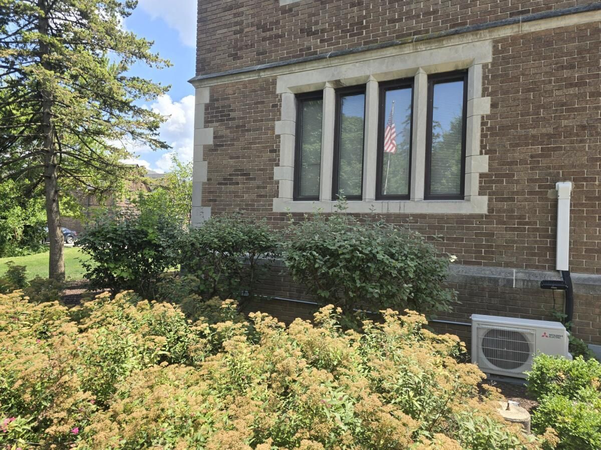 Brick building with window and landscaping; air conditioner unit on the right.