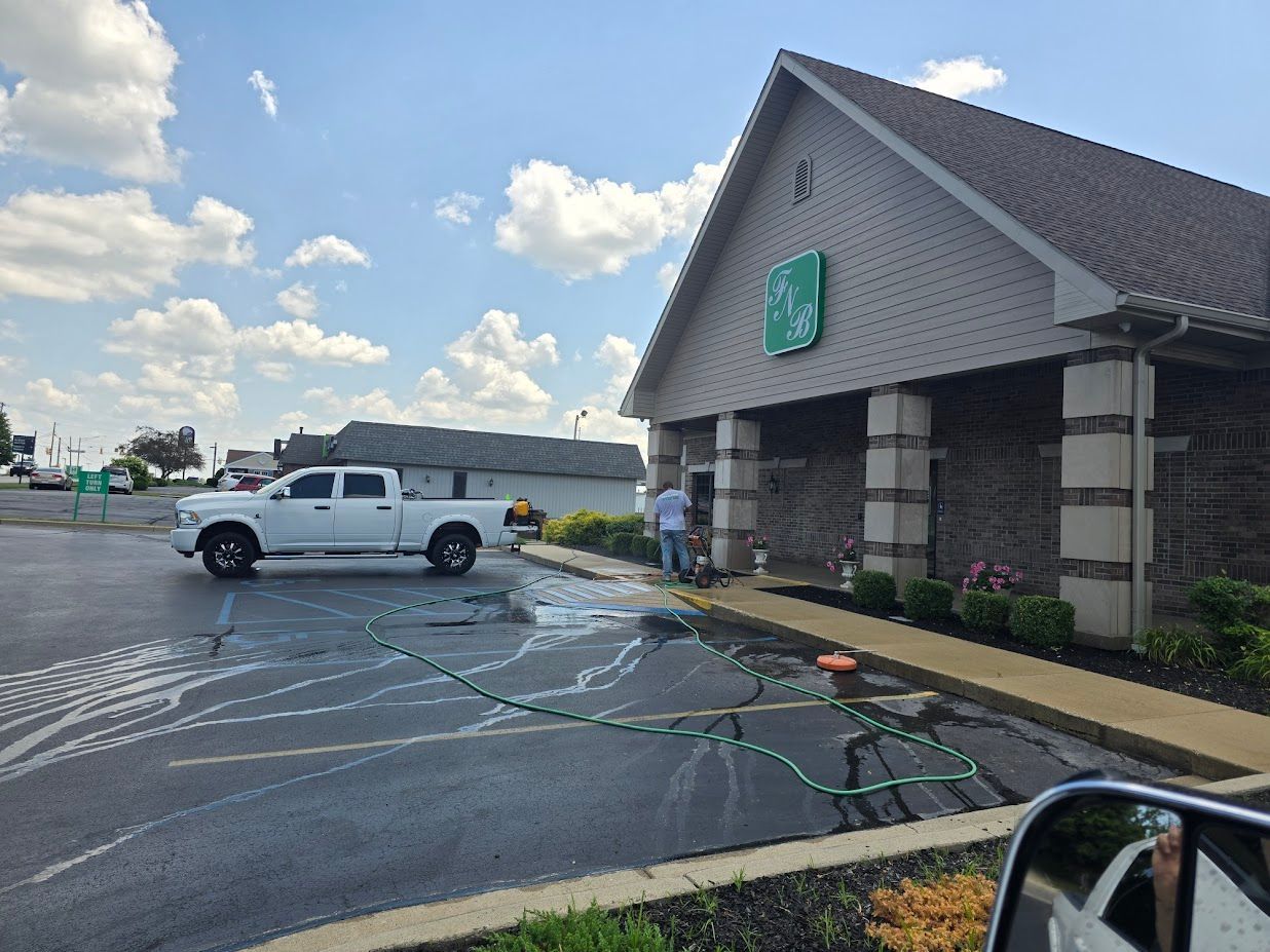 White pickup truck parked near a building with a green sign. A person is washing the building's exterior with a hose.
