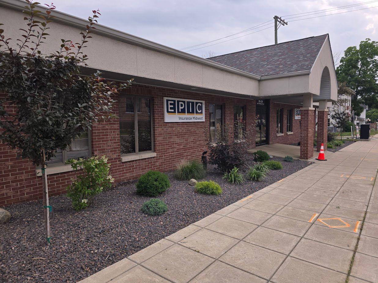 A brick building with a sign that reads EPIC, flower beds, and a sidewalk.