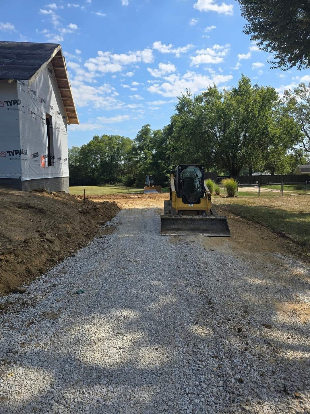 Gravel path leading to a building under construction; a skid steer sits on the path.