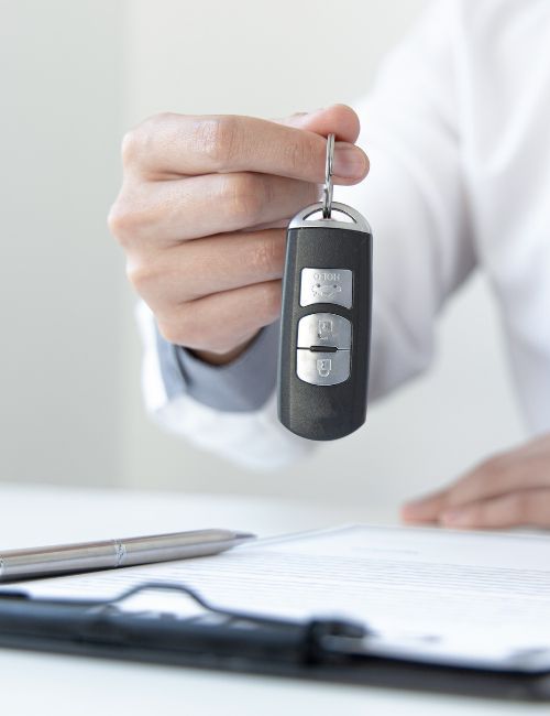 a person is holding a car key over a clipboard after approving a car loan.