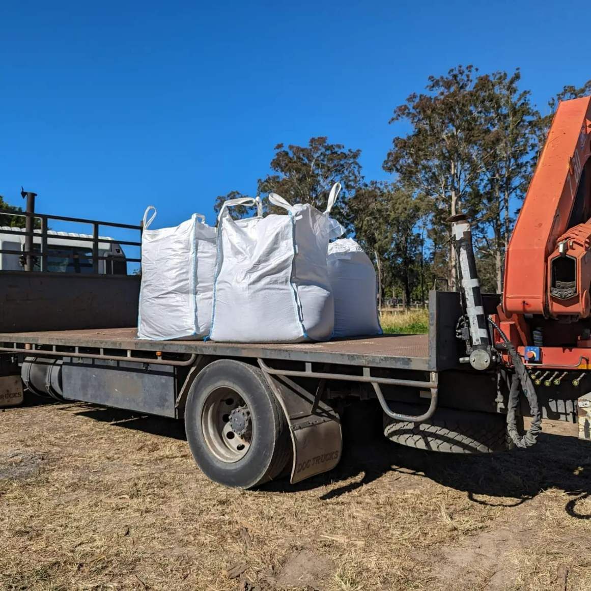 A Flatbed Truck With a Crane Attached to It is Parked in a Field — HKL Landscape Supplies in Taree, NSW 