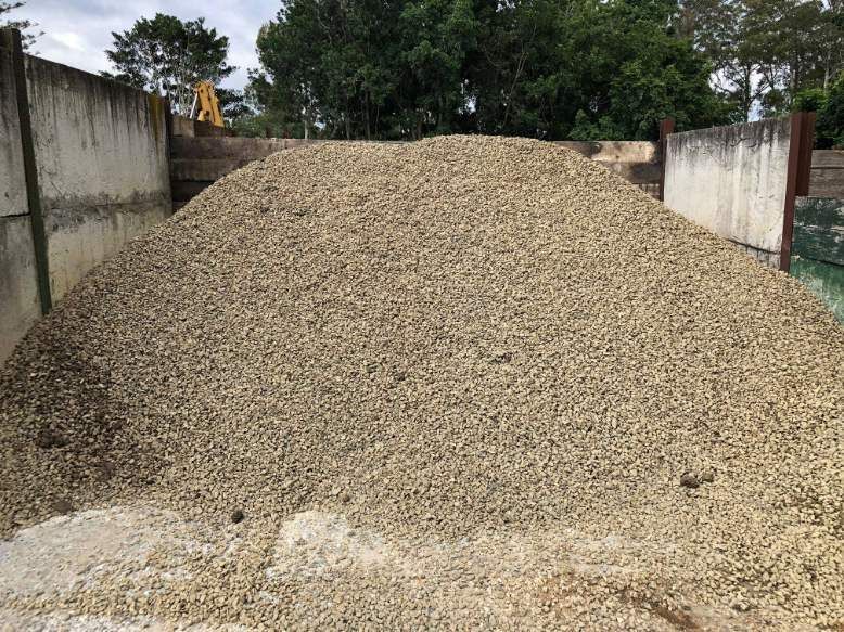 A Large Pile Of Gravel Is Sitting In Front Of A Concrete Wall — HKL Landscape Supplies in Taree South, NSW