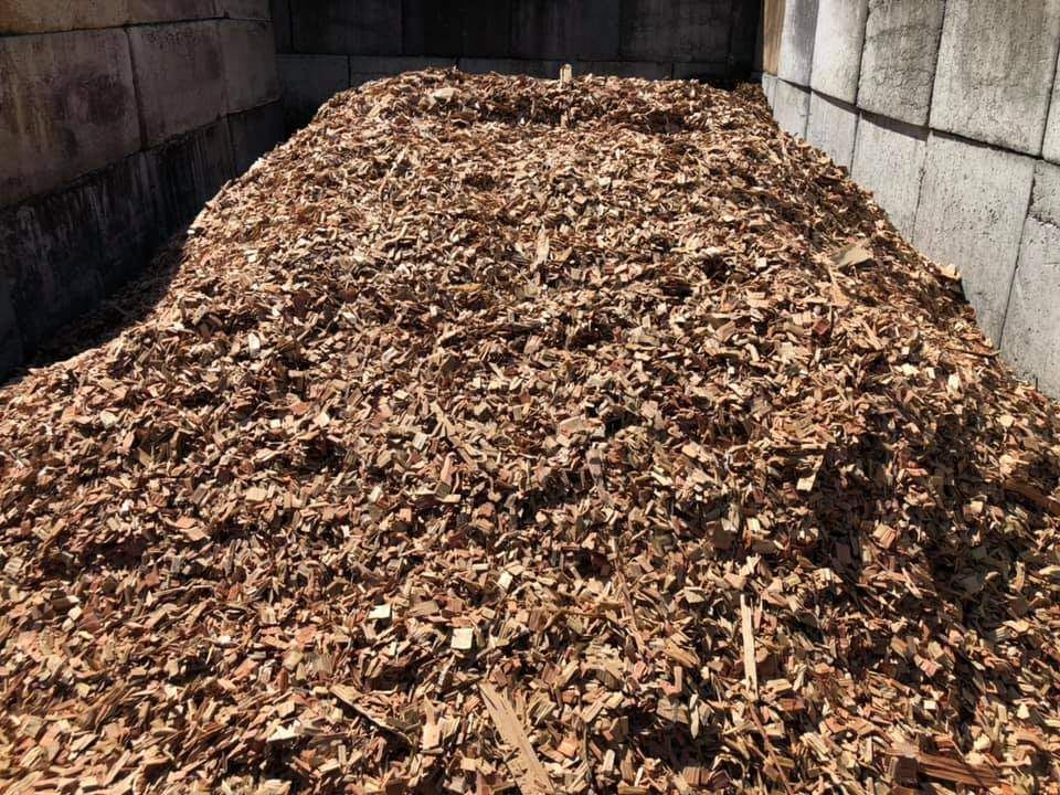 A Pile Of Wood Chips Is Sitting In Front Of A Brick Wall — HKL Landscape Supplies in Taree South, NSW