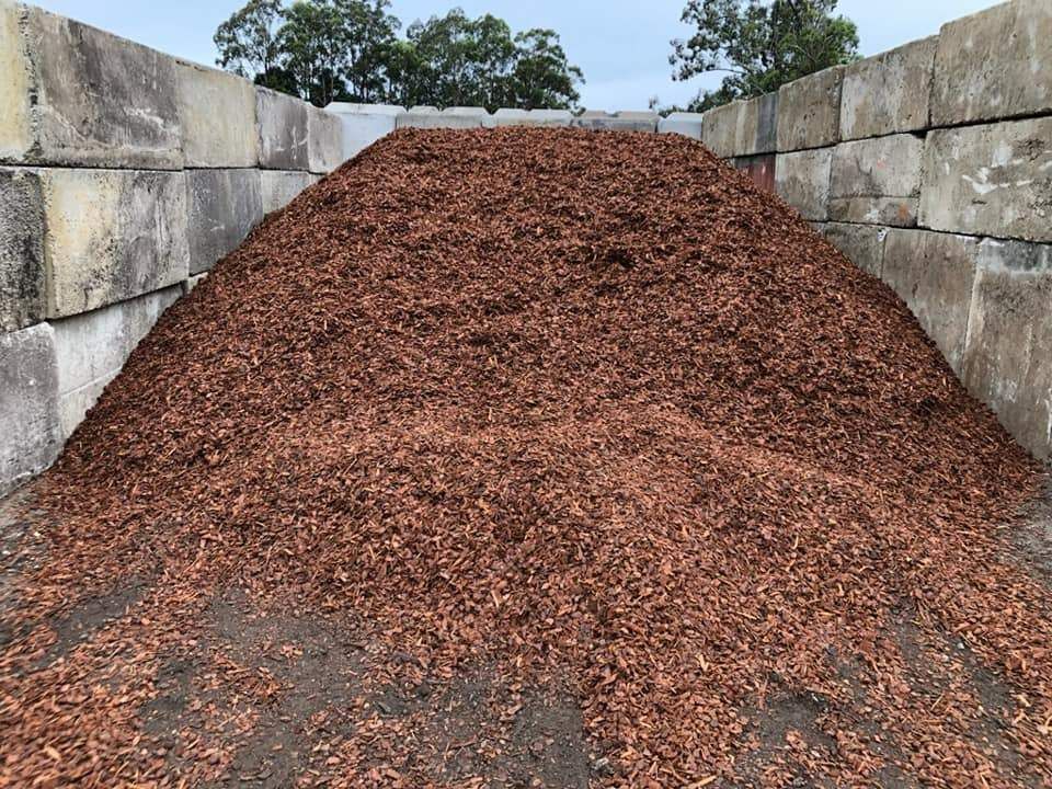 A Pile of Brown Mulch is Sitting in Front of a Brick Wall — HKL Landscape Supplies in Smiths Lake, NSW