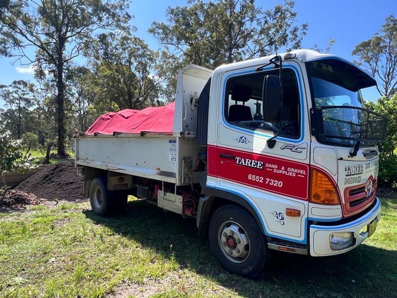 A Dump Truck With a Red Tarp on the Back is Parked in a Grassy Field — HKL Landscape Supplies in Wingham, NSW
