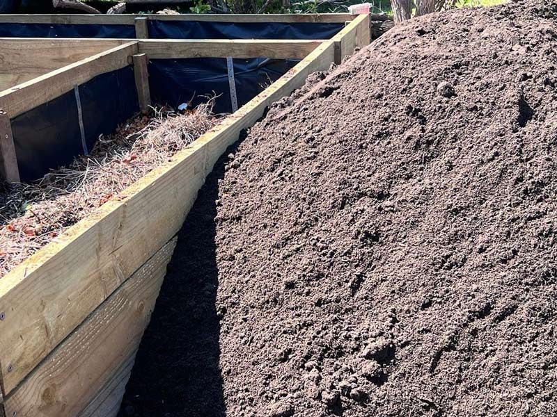 A Pile of Dirt is Sitting Next to a Wooden Fence — HKL Landscape Supplies in Gloucester, NSW 