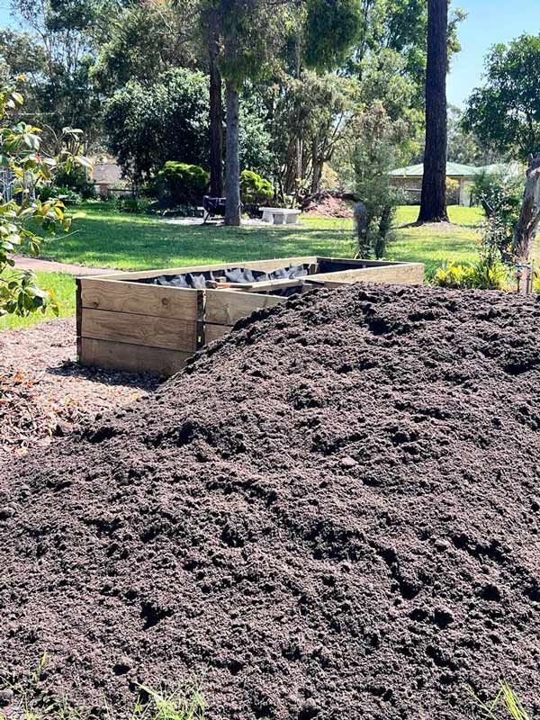 A Pile of Dirt is Sitting in a Yard Next to a Wooden Box — HKL Landscape Supplies in Nabiac, NSW 