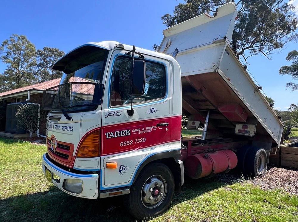 A Dump Truck is Parked in the Grass in Front of a House — HKL Landscape Supplies in Tuncurry, NSW 