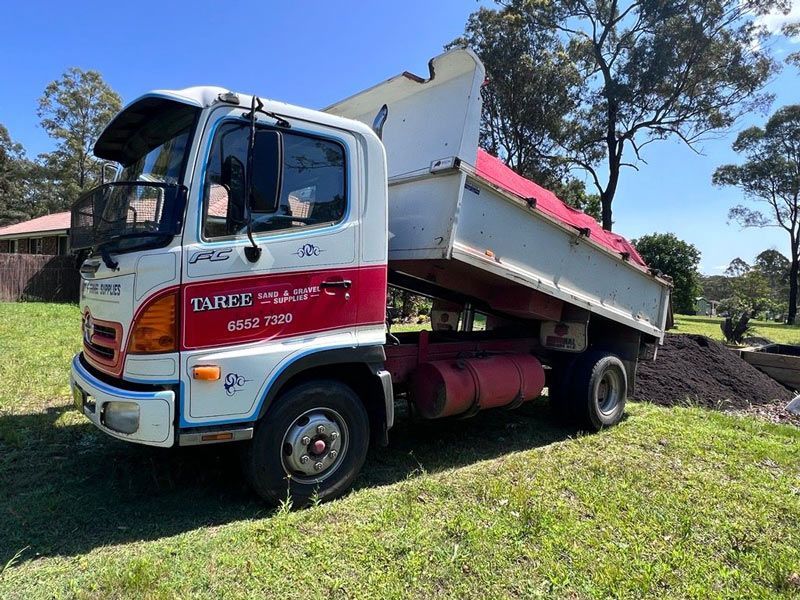An Orange Dump Truck Is Driving Down A Dirt Road — HKL Landscape Supplies in Taree South, NSW