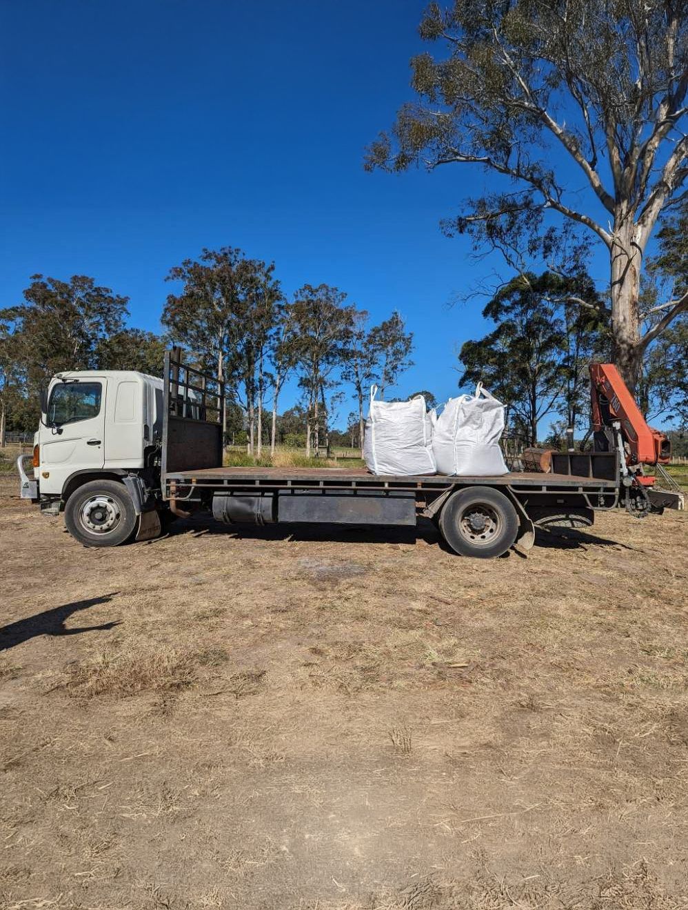A Flatbed Truck With a Crane Attached to It is Parked in a Field — HKL Landscape Supplies in Coolongoolook, NSW