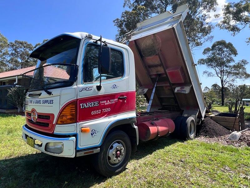 A White and Red Dump Truck is Parked in a Grassy Field — HKL Landscape Supplies in Old Bar, NSW