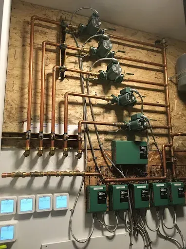 Wall-mounted boiler heating system with five circulating pumps and control modules connected by copper piping.