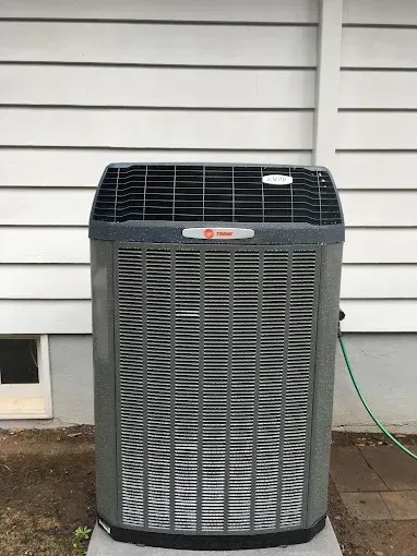 A grey Trane air conditioning unit sitting on a concrete pad against white horizontal house siding.