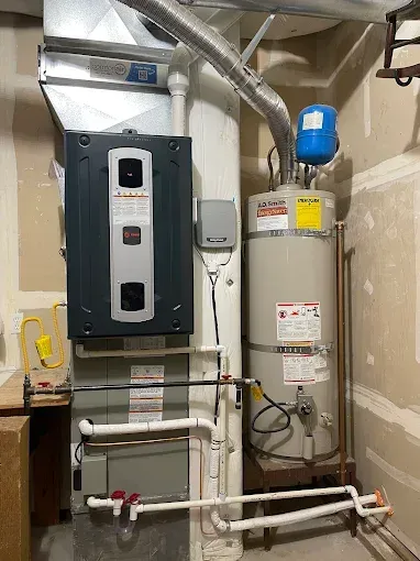 A gas furnace and a water heater with attached plumbing and ductwork installed in a utility closet.