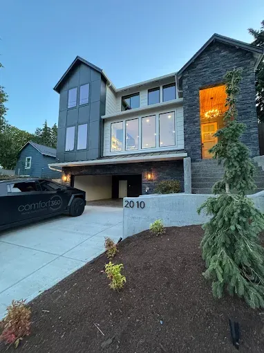 A modern two-story home with a dark stone exterior and gray siding at twilight, featuring an attached garage and driveway.